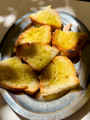 an image of 6 slices of fettunta–toasted bread with olive oil and garlic–on a silver platter in the dappled sun