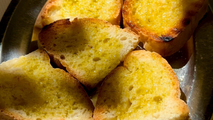 an image of 6 slices of fettunta–toasted bread with olive oil and garlic–on a silver platter in the dappled sun
