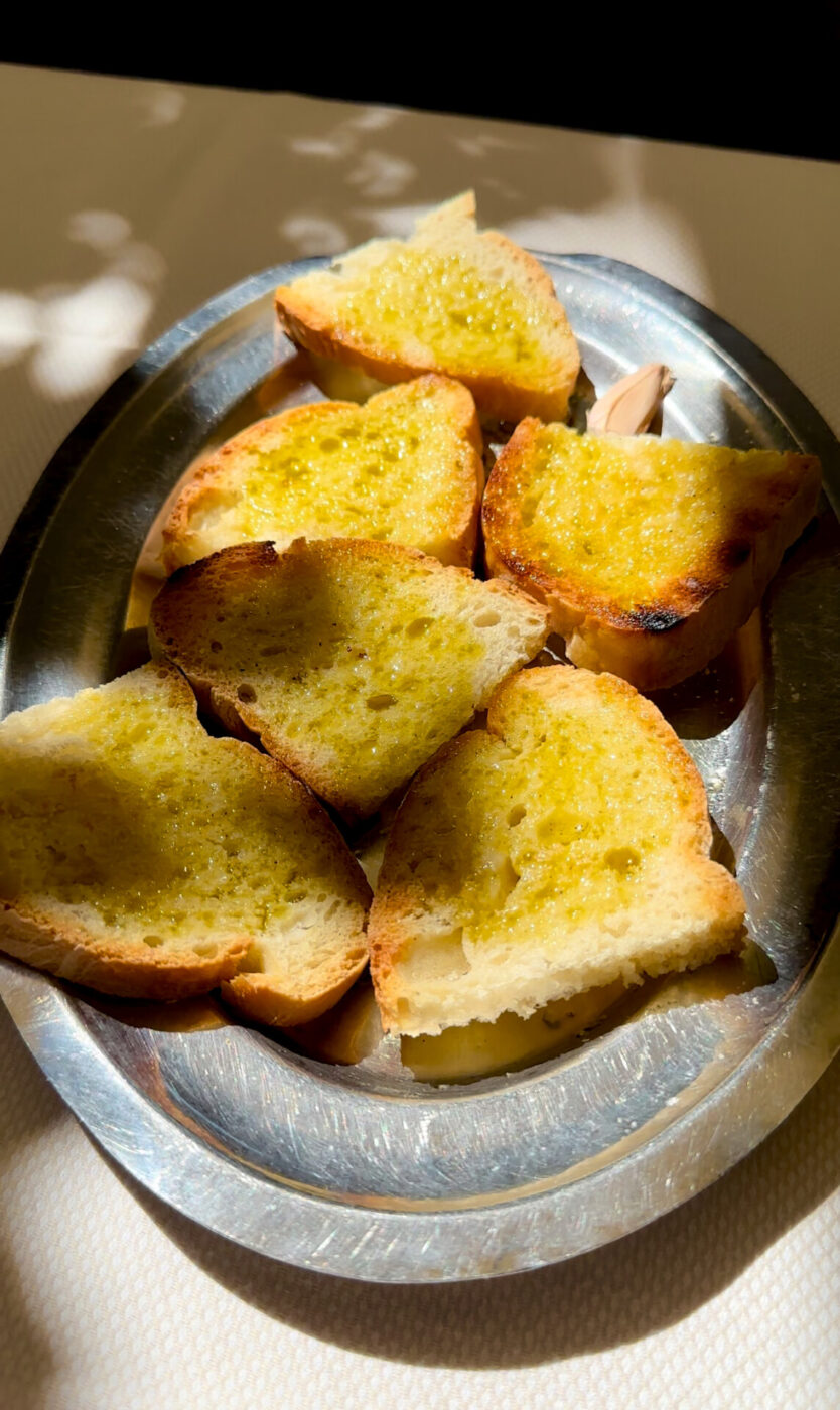 an image of 6 slices of fettunta–toasted bread with olive oil and garlic–on a silver platter in the dappled sun