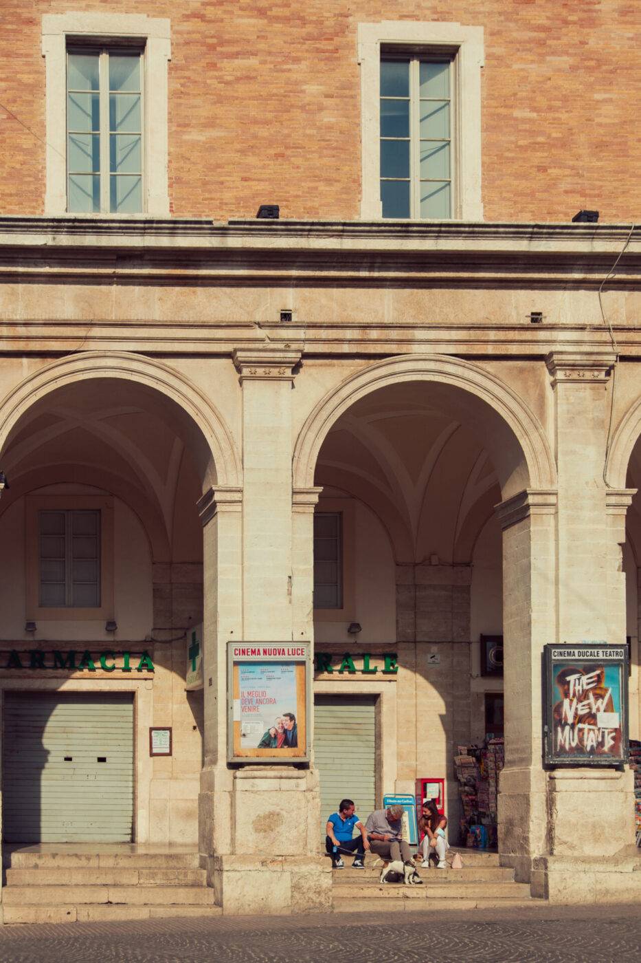 an image of people sitting on steps under arched porticos in Urbino Marche