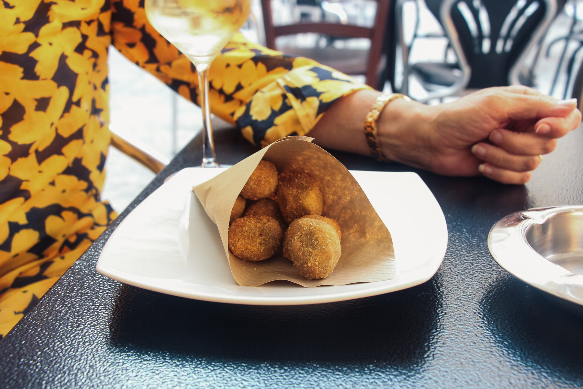 a cone of fried olives on a plate next to a glass of white wine