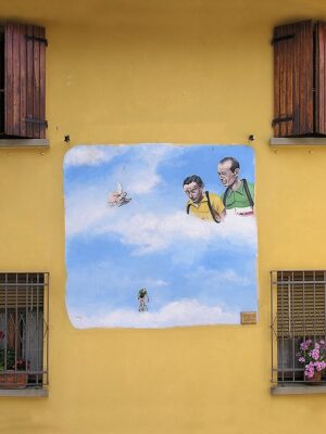 a yellow wall in Dozza with a square mural that's two guys looking down in a blue sky