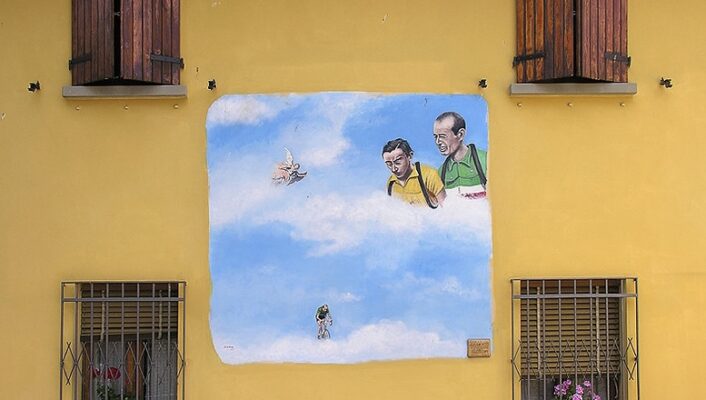 a yellow wall in Dozza with a square mural that's two guys looking down in a blue sky