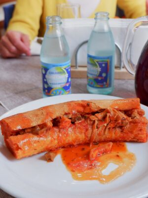an image of a morzello sandwich in Calabria, a read meaty stew inside a long slice of bread with the sauce spilling out onto the plate