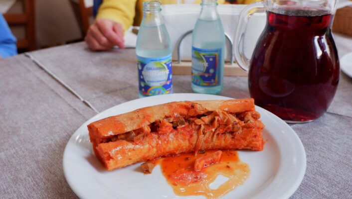 an image of a morzello sandwich in Calabria, a read meaty stew inside a long slice of bread with the sauce spilling out onto the plate