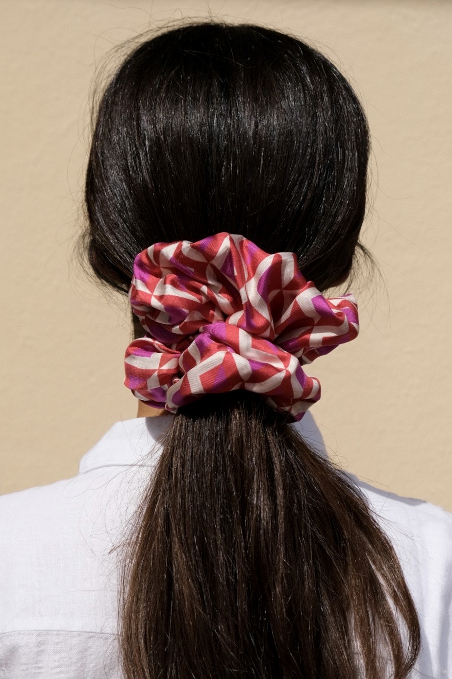 A woman from the back with her dark brown hair in a pink and purple scrunchie