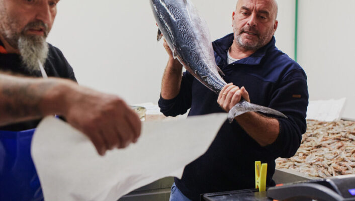 a man lifting a giant fish to place on a scale at the milan fish market