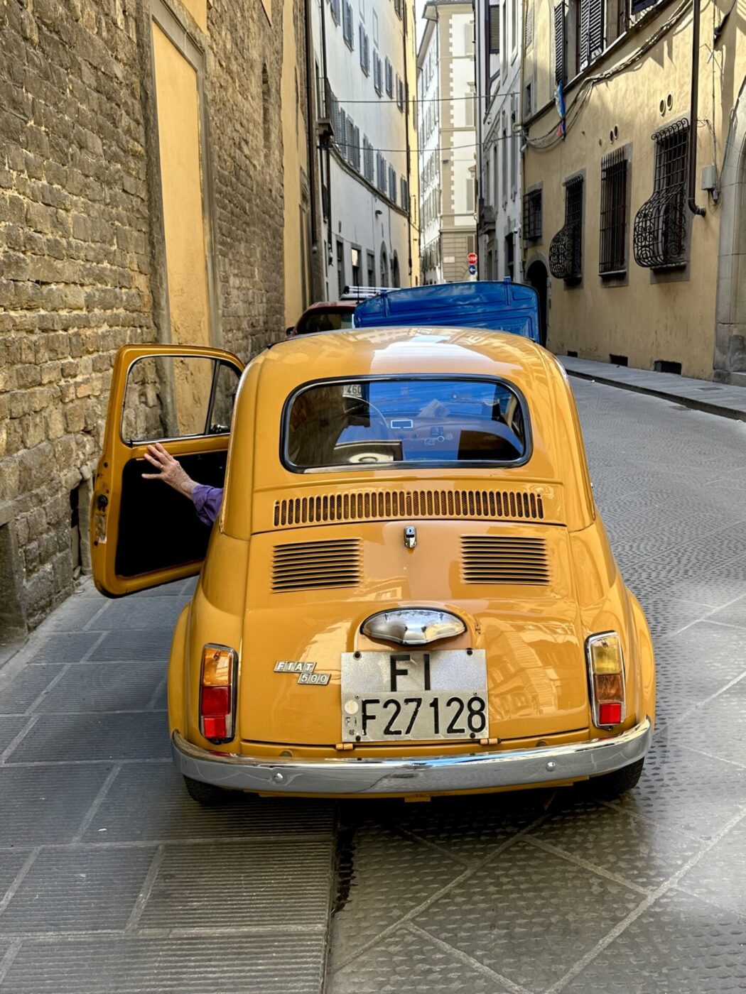 a small bright yellow orange car on an Italian street