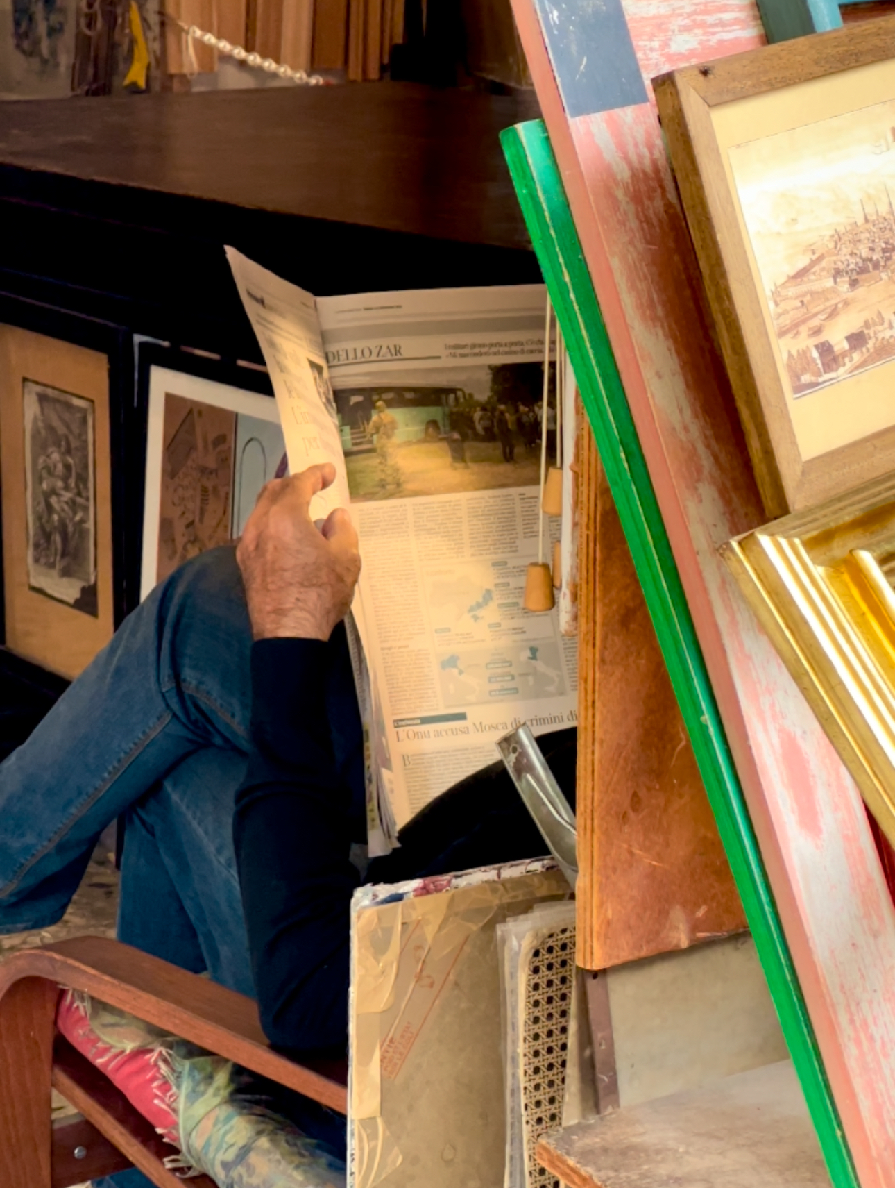 a man reading a newspaper and sitting in a shop where he frames things