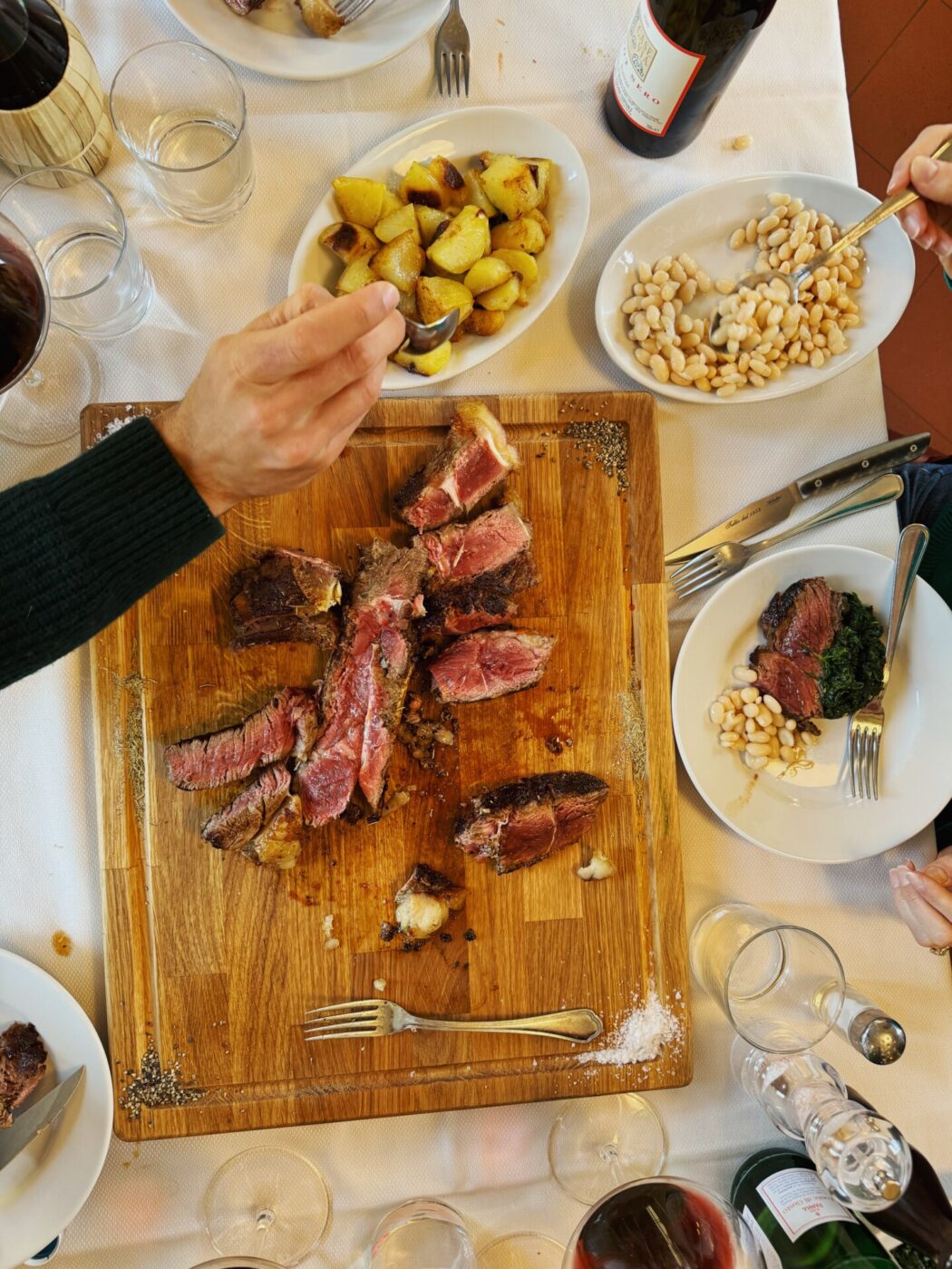 an overhead image of Da Tullio with a cutting board filled with steak and sides of beans and potatoes