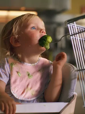 an image of a young girl in a high chair eating broccoli being fed to her by a supermarket basket from Coop's 2023 Ad