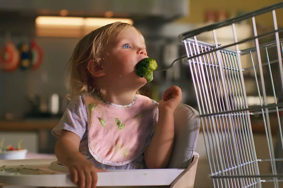 an image of a young girl in a high chair eating broccoli being fed to her by a supermarket basket from Coop's 2023 Ad