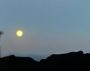 an image of the bright white moon against a light blue sky over rooftops in Tuscany