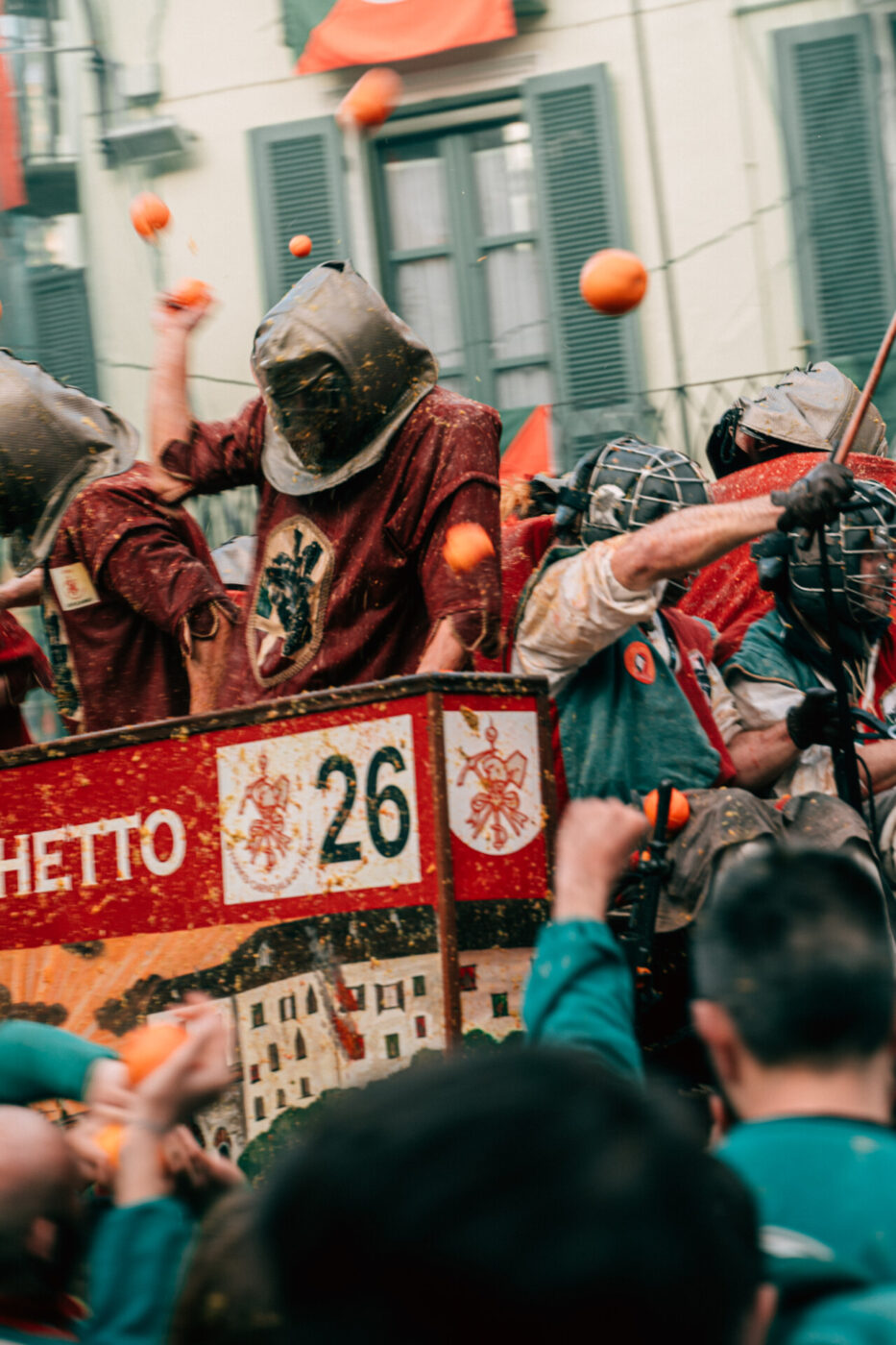 an image of a man wearing a black masked hood riding on the carriage and having oranges thrown at him