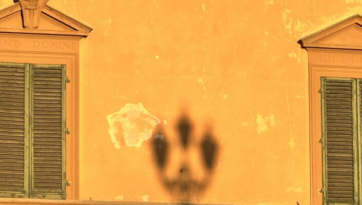 an image of the shadow of a lamppost against a bright yellow wall in Florence