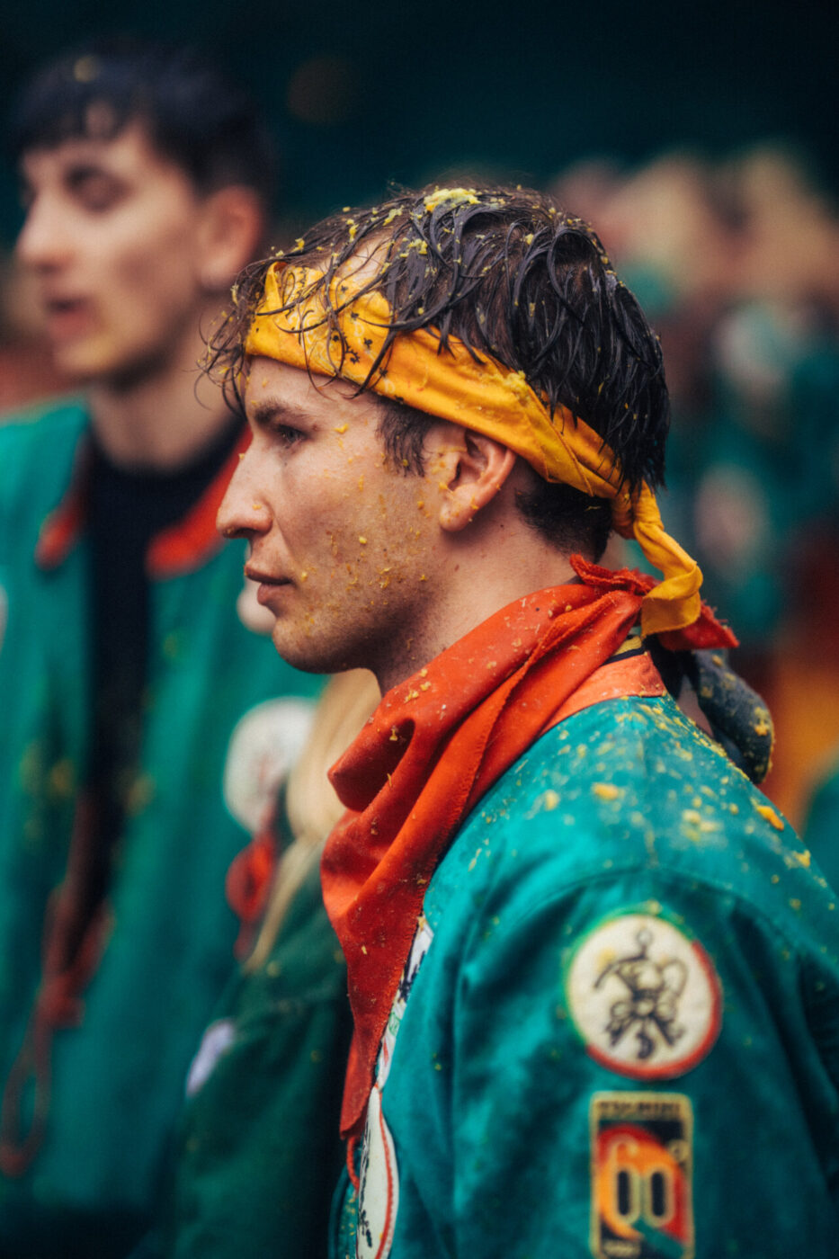 a young man in Ivrea wearing a green jacket covered in orange pulp