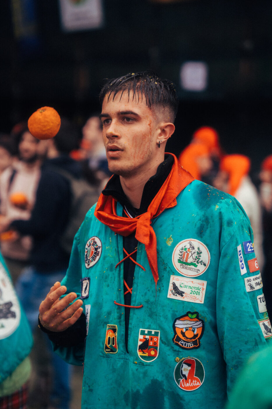 an image of one of the orange throwers during the ivrea festival with a green jacket and completely covered in orange