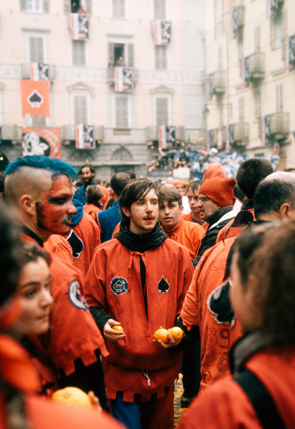 an image of a group of men wearing orange jackets and holding oranges with bloody noses and ready to throw them