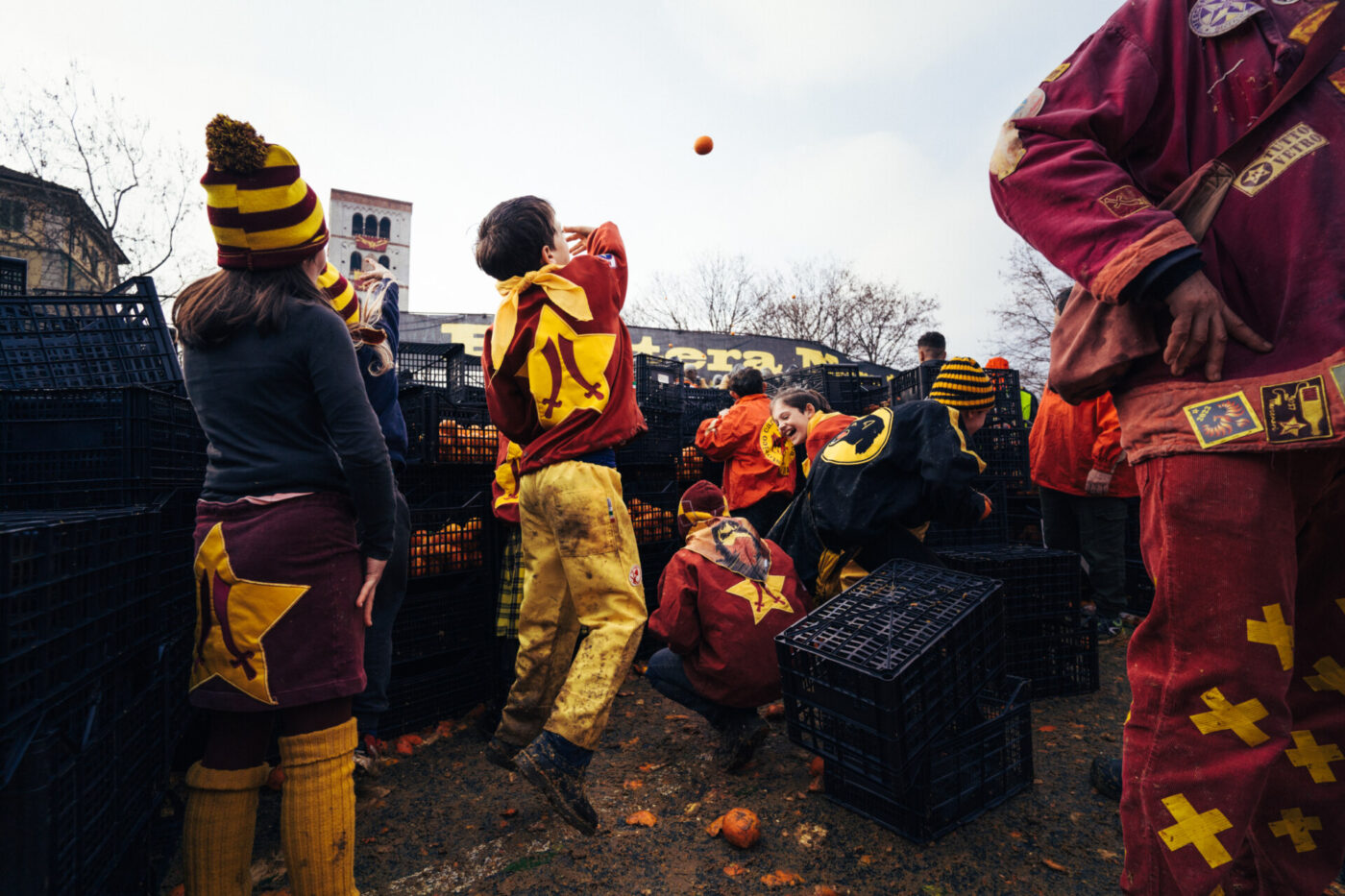 an image of people crouched below black crates in Ivrea and one boy throwing an orange