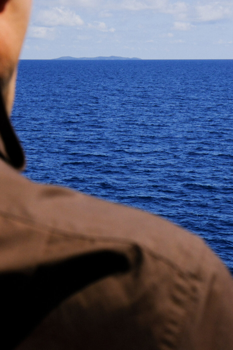 an image from behind of a man looking out at the sea