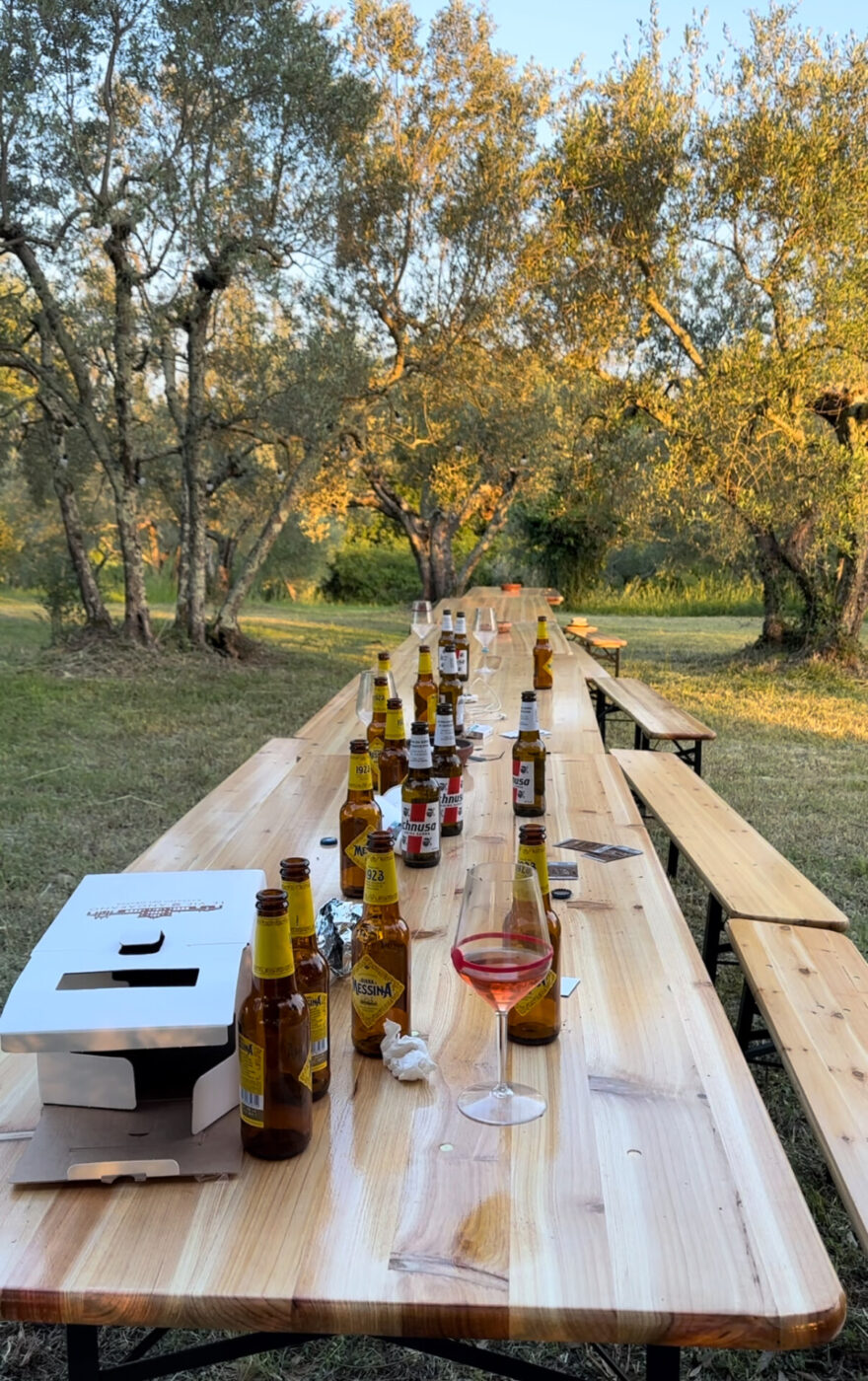 a long wooden picnic table outside filled with empty beer bottles