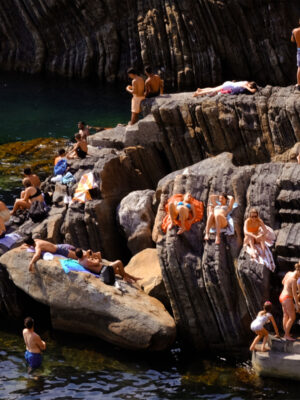 People laying along rocks by the sea in Liguria Ponente