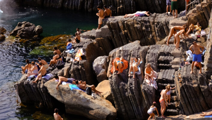 People laying along rocks by the sea in Liguria Ponente