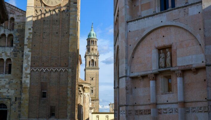 an image of a a tall bell tower between roofs and buildings in Parma