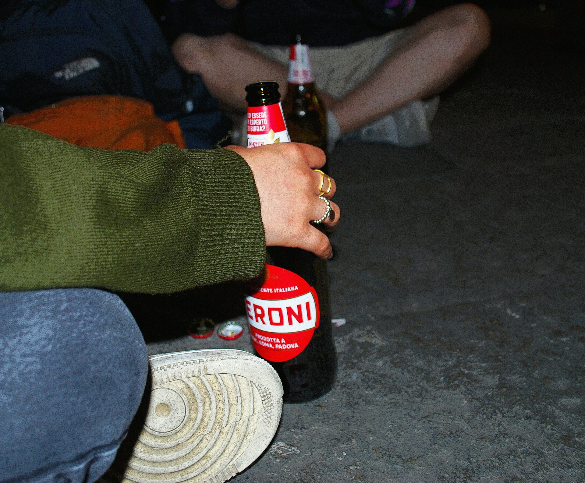 an image of people sitting on the ground outside holding a peroni