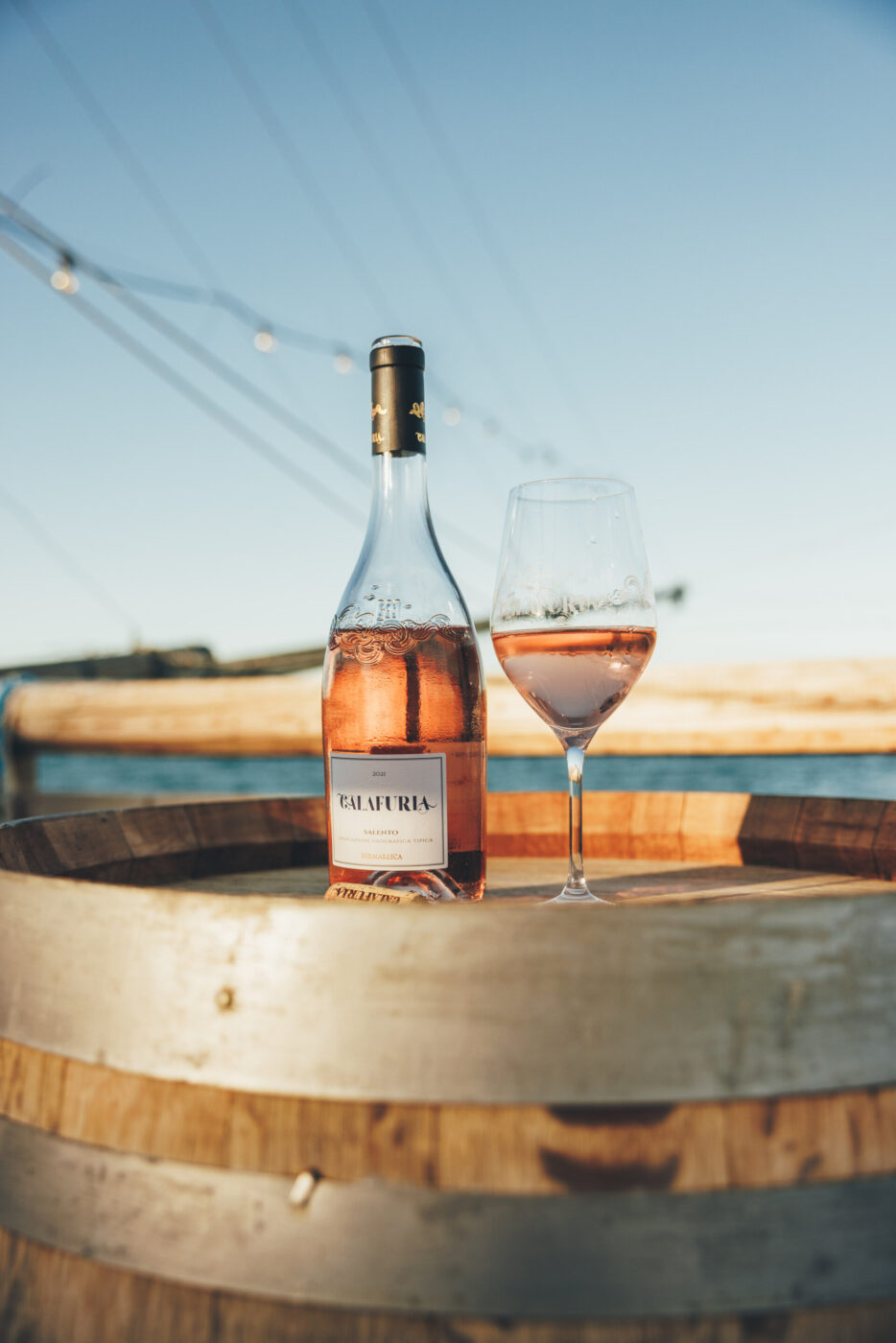 a bottle of rose sitting on a barrel at sunset on Trabucco Tormaresca