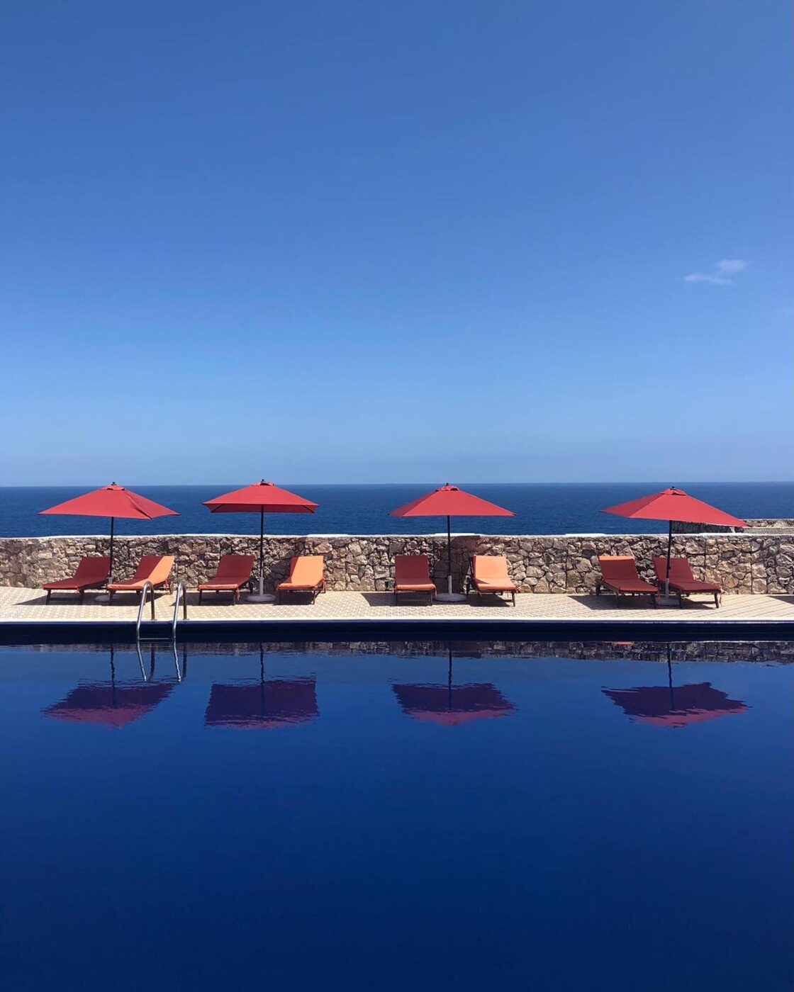 the blue pool with orange umbrellas and lounge chairs with the blue sea beyond it at piccolo mondo