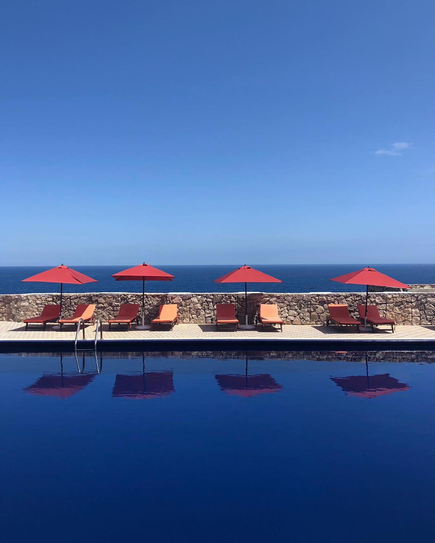 the blue pool with orange umbrellas and lounge chairs with the blue sea beyond it at piccolo mondo