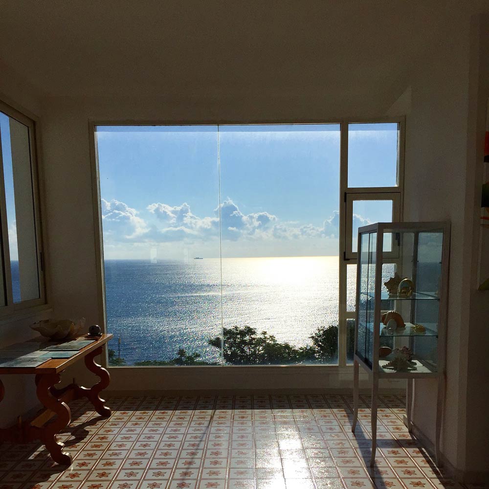 an image of the blue sea photographed through a large glass window in the lobby of Piccolo Mondo hotel