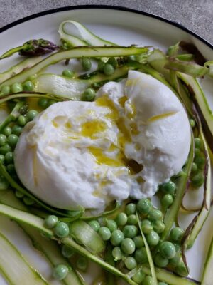 an image of a cut open, oozing burrata on top of a pea and shaved asparagus salad with olive oil