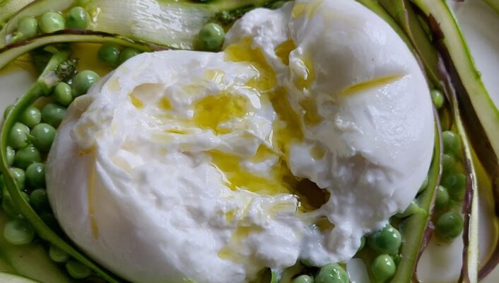 an image of a cut open, oozing burrata on top of a pea and shaved asparagus salad with olive oil