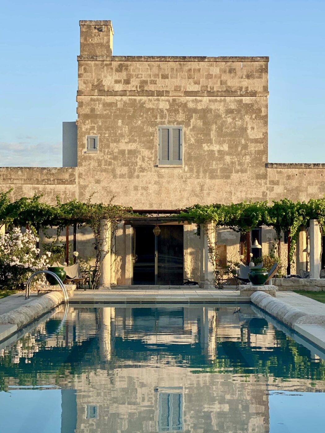 an image of the pool at Masseria Schiuma in front of grapevine covered pergolas and the tan, two story masseria