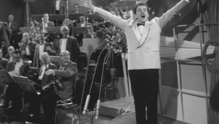 a black and white image of Domenico Modugno singing with his arms raised