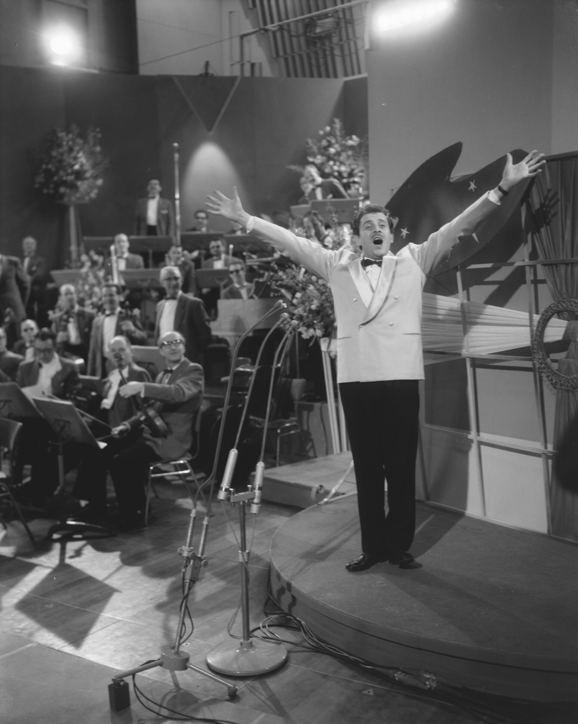 a black and white image of Domenico Modugno singing with his arms raised