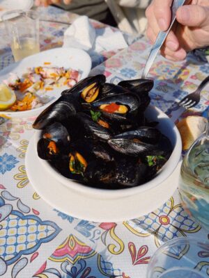 an image of cozze alla tarantina in a bowl on a patterned tablecloth in the sun outside in Puglia