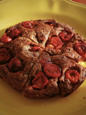 a close up image of a round of focaccia barese studded with tomatoes sliced into pieces like a cake