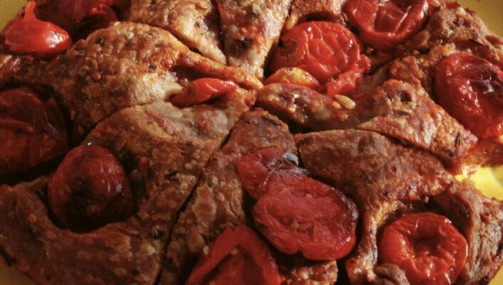 a close up image of a round of focaccia barese studded with tomatoes sliced into pieces like a cake