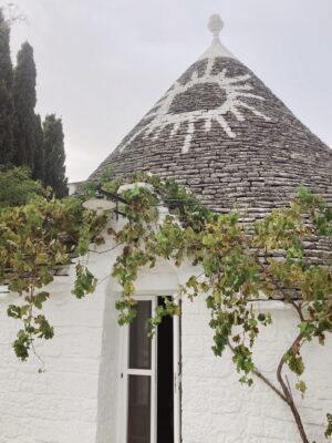 a white conical trullo in Puglia with a white painted symbol of a sun on the gray rocky roof