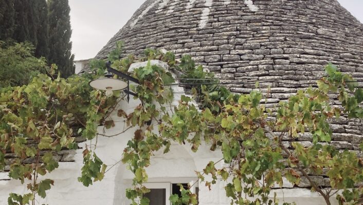a white conical trullo in Puglia with a white painted symbol of a sun on the gray rocky roof