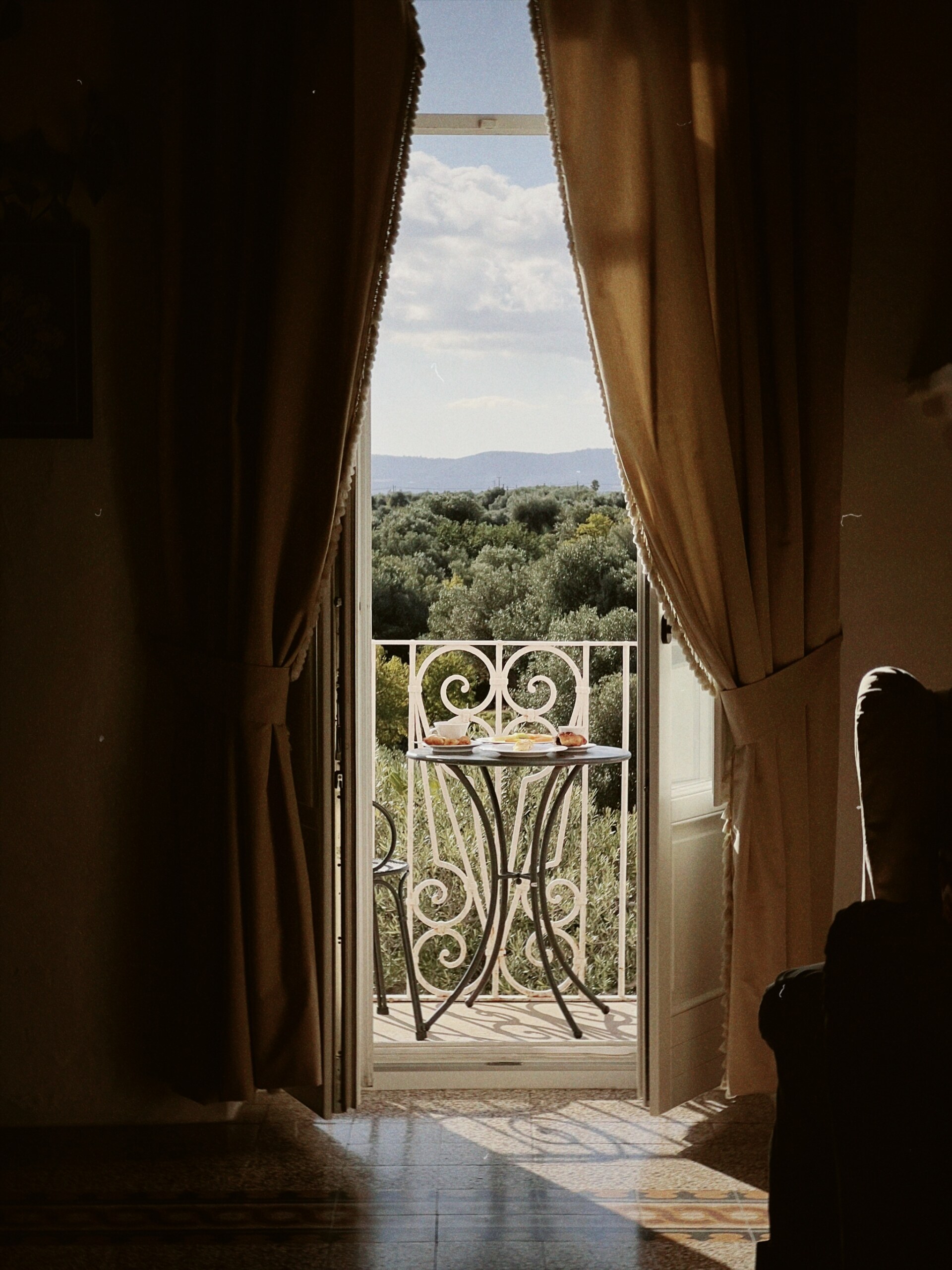 an image from inside a room out to the balcony with a small table set with breakfast overlooking olive trees at Masseria Torre Coccaro