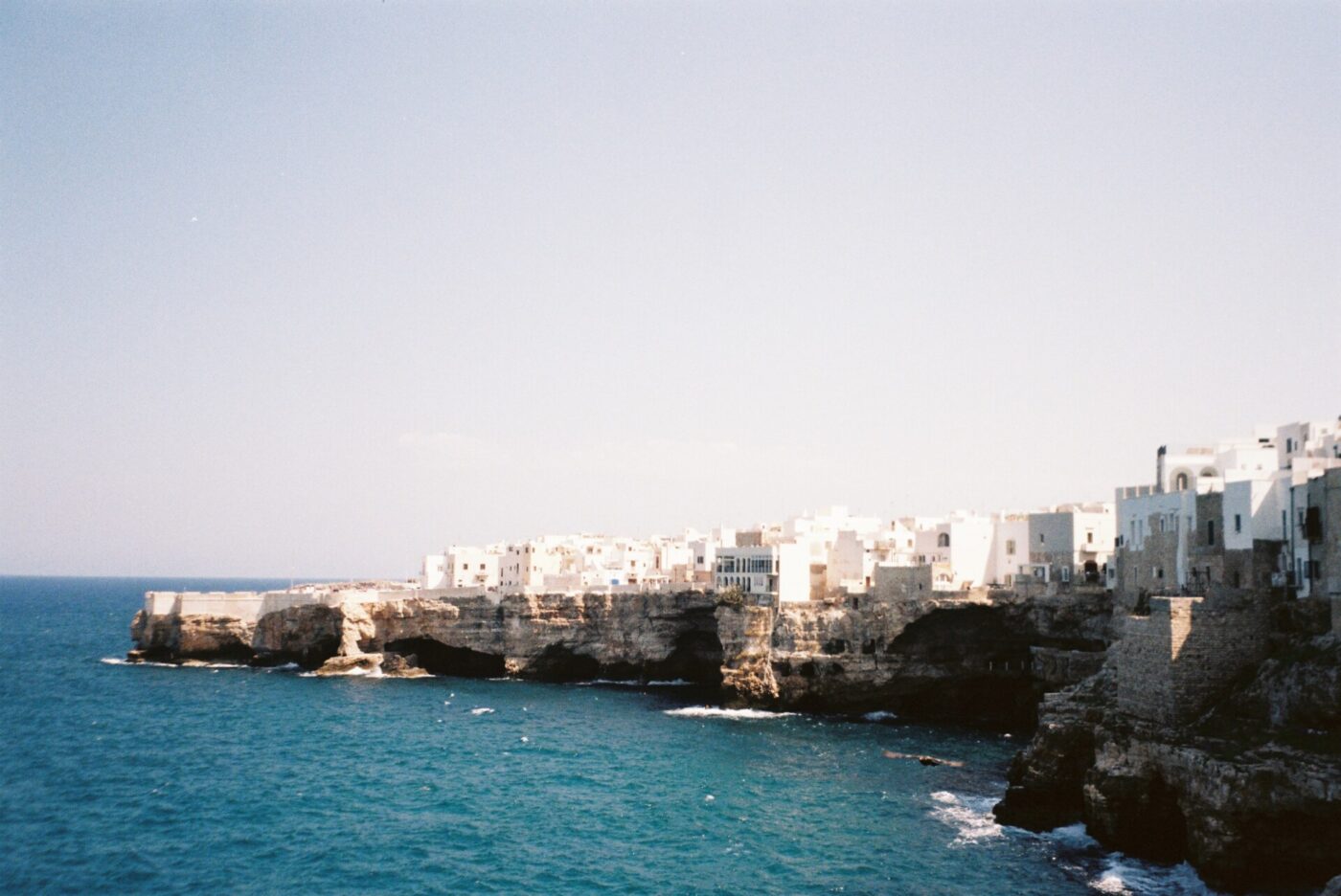 a film photo of Polignano a Mare taken from a far to see the white town dangling on the cliff
