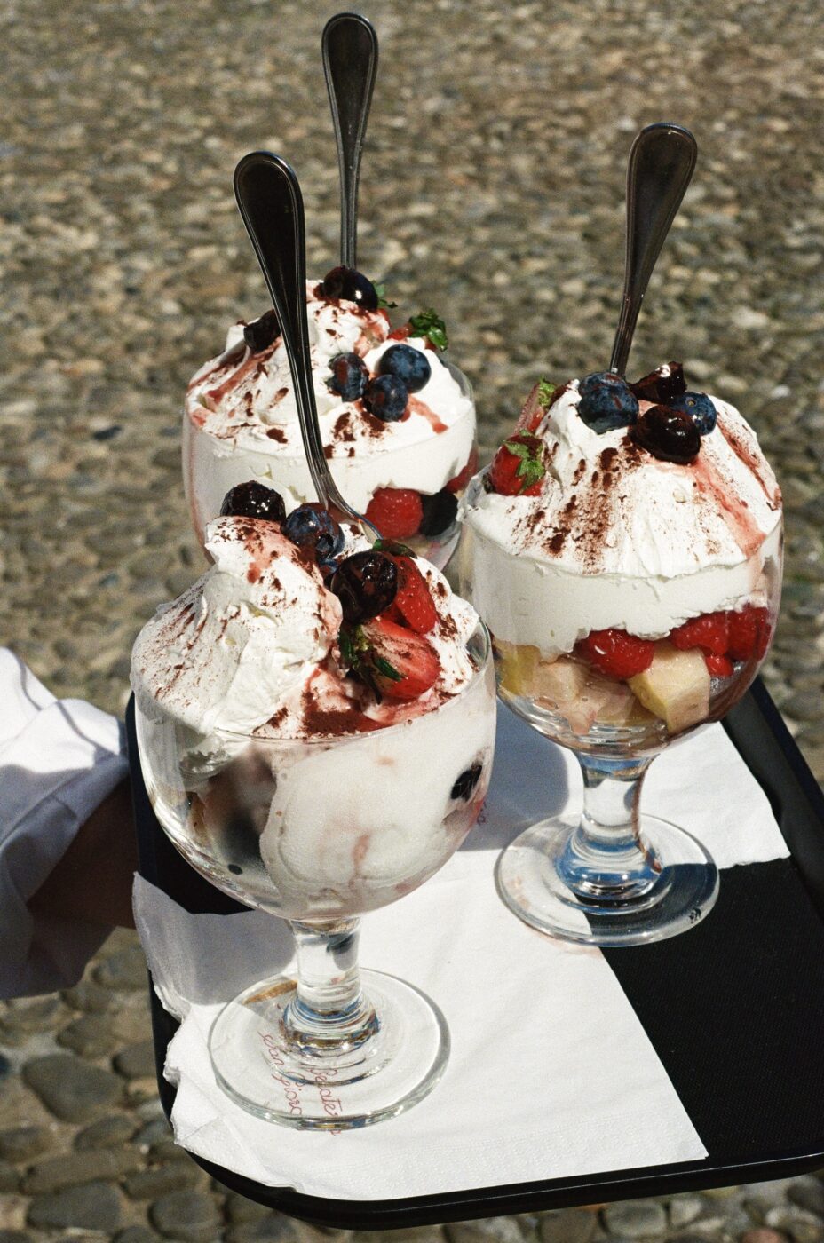 a close up of three paciugo, ice cream sundaes, on a tray carried by a waiter