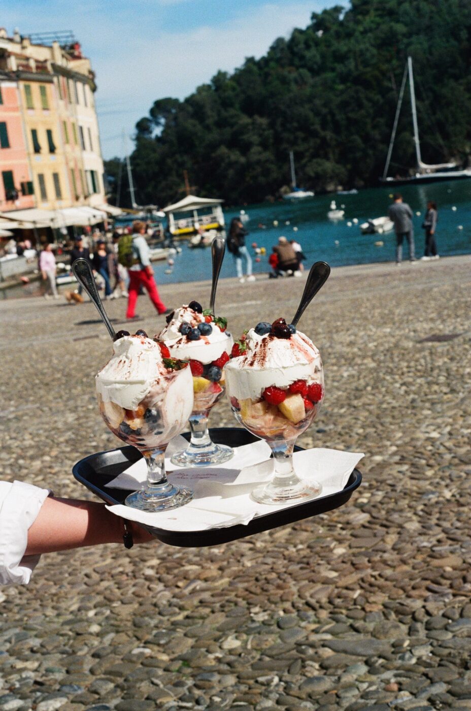 an image of a server carrying a tray of three paciugo, ice cream sundaes, in the piazza at portofino