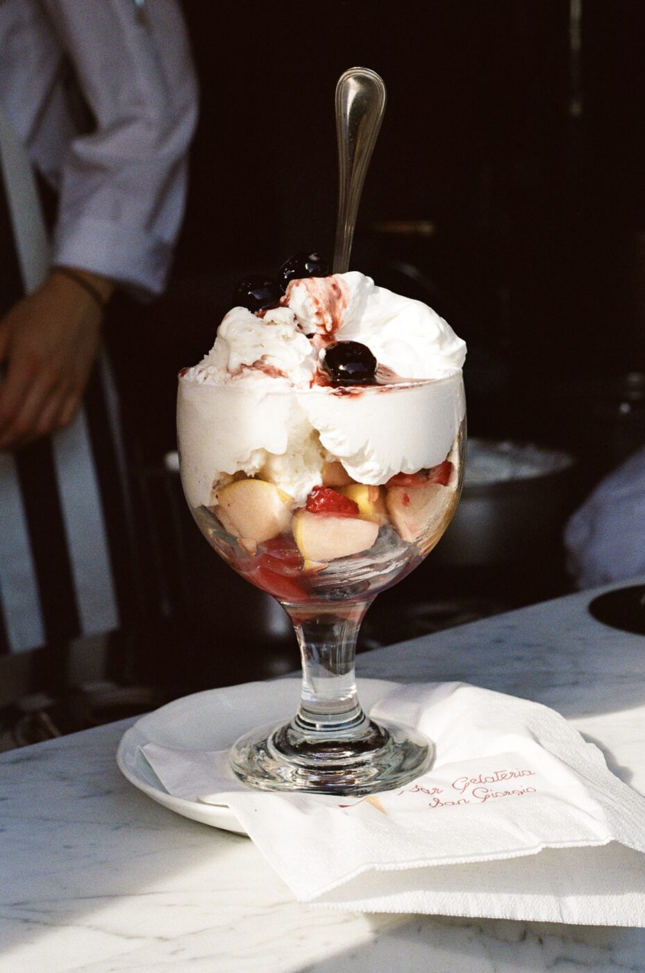 a close up of a glass filled with gelato and fresh fruit and whipped cream, called a paciugo