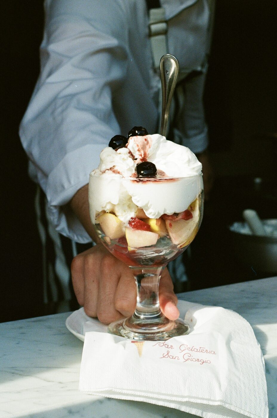 a man handing a paciugo, ice cream sundae, through a window with a napkin that says Bar Gelateria San Giorgio