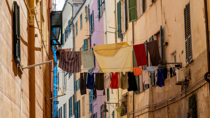 a thin street in Savona with tall colorful houses and laundry hanging between